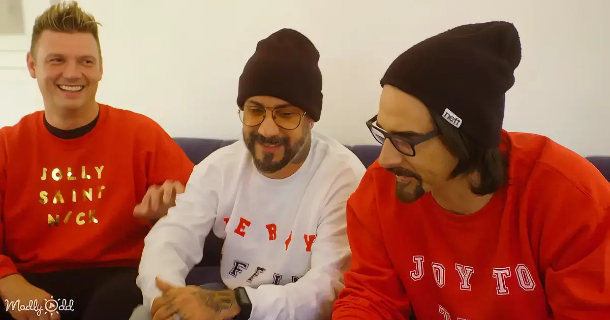 Three men in red and white shirts, one smiling, two wearing beanie hats, sitting on a couch.