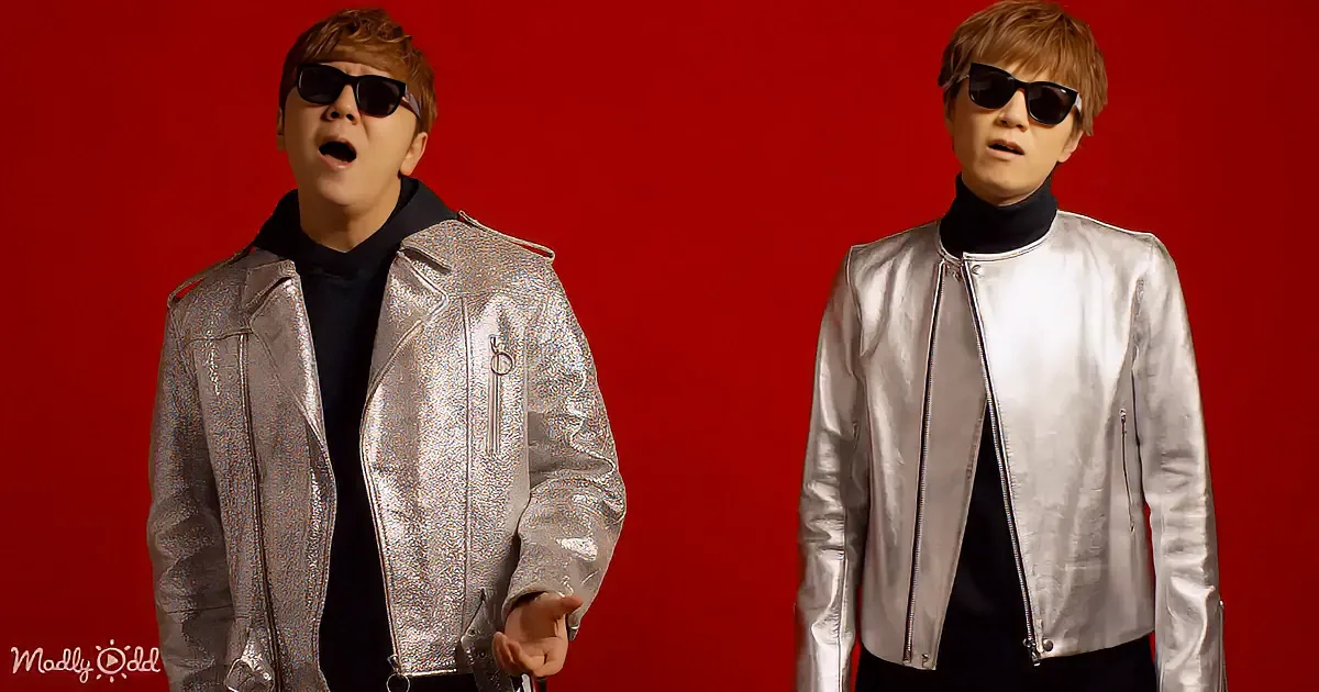 A person in a shiny silver jacket and black turtleneck poses against a red background.