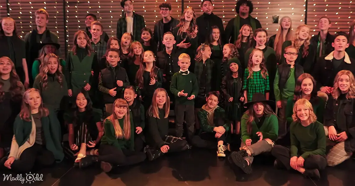 A group of children and adults in green and black attire pose together on a stage.