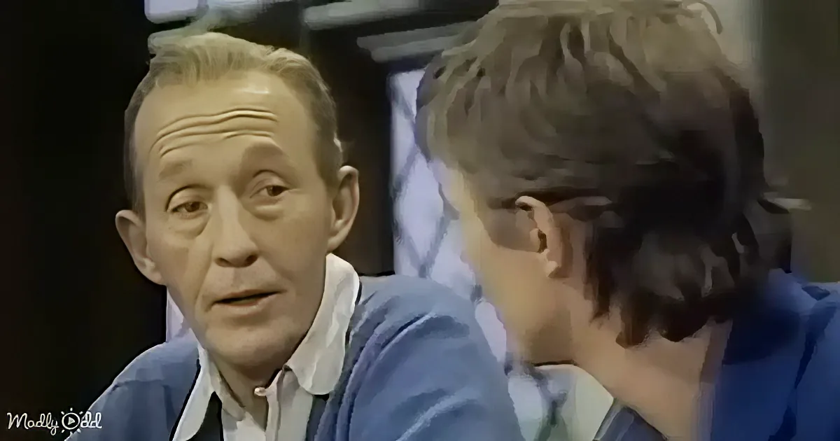 Two men in a dimly lit room, one in a blue suit, the other in a blue sweater, appear to be in a serious conversation.
