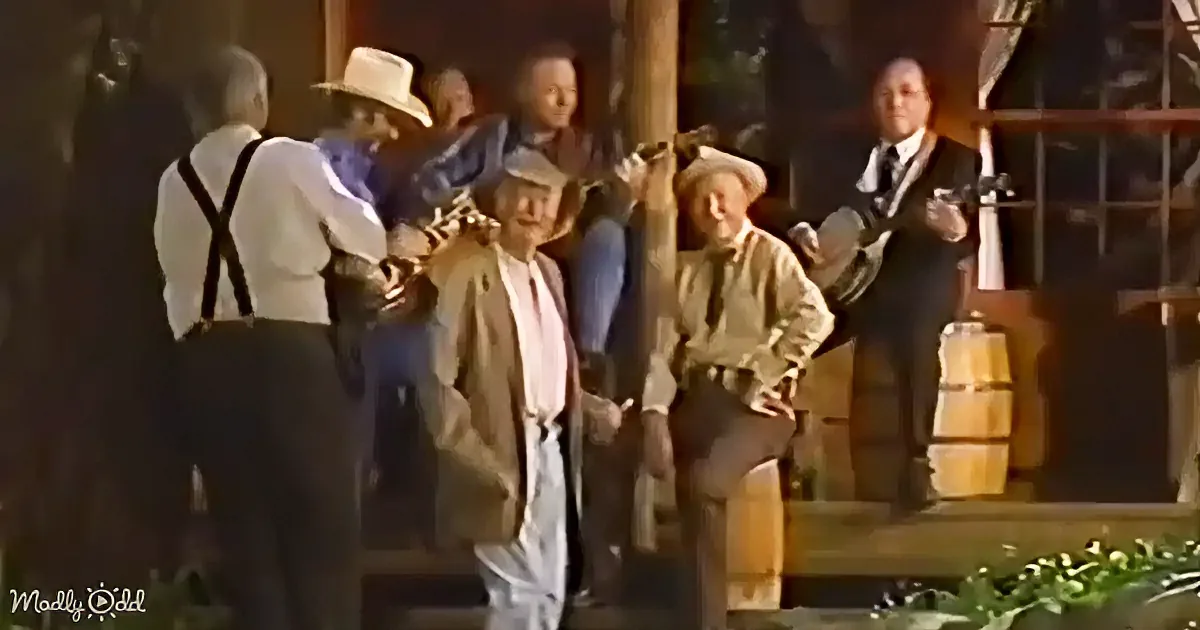 A man in a white shirt and suspenders is dancing with others in a rustic setting, possibly a barn or stage.