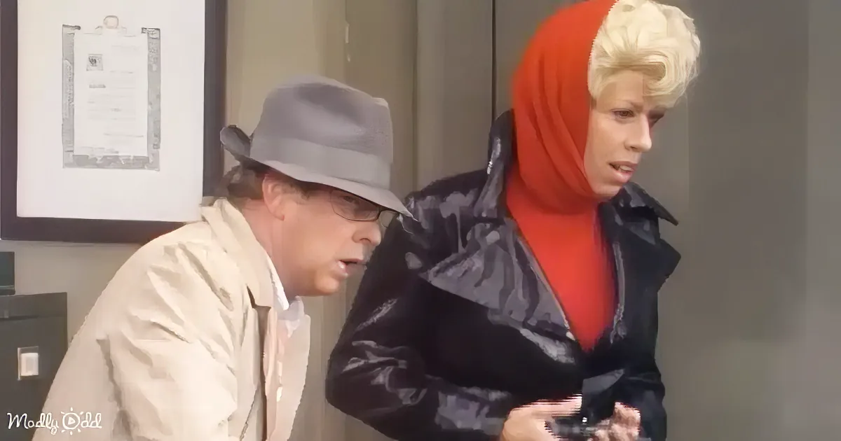 A man in a fedora and beige jacket sits next to a woman in a red headscarf and black jacket, both appearing to be in a room.