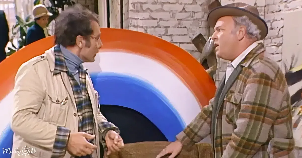 Two men in plaid shirts and jackets are engaged in a conversation, one holding a brown object.