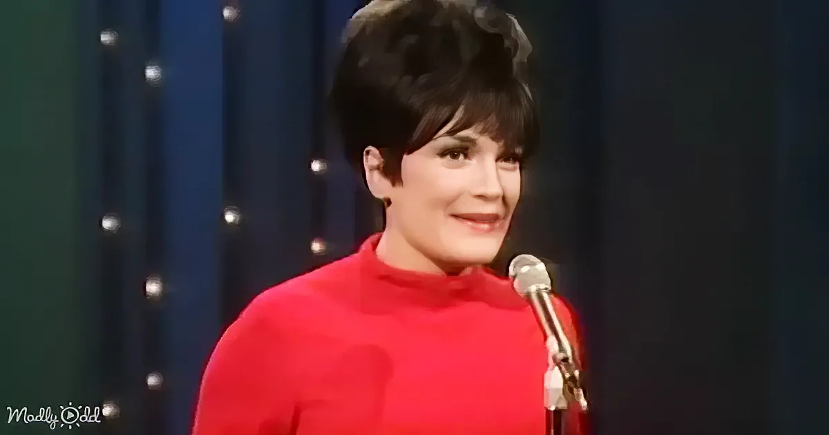 A woman in a red turtleneck smiles near a microphone against a dark backdrop.