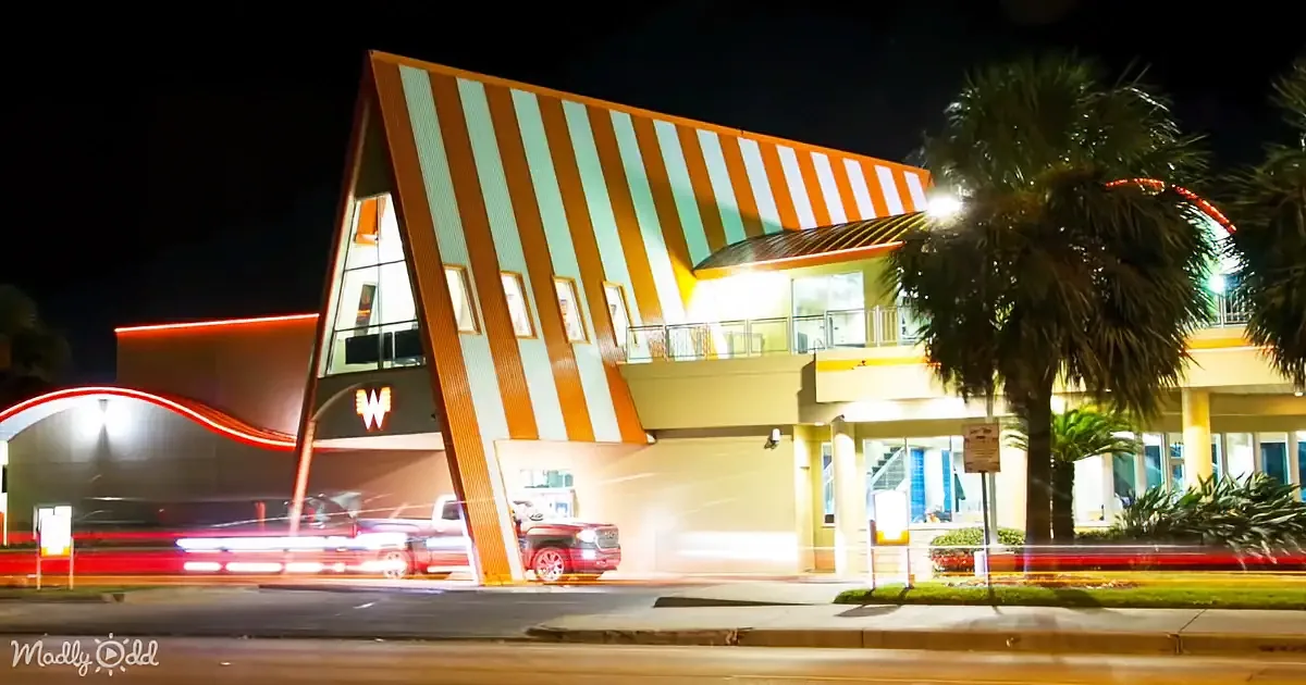 A brightly lit, modern building with orange and white stripes and a red truck in front, set against a night sky.