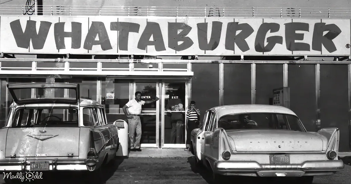 A vintage Whataburger sign with two cars and people in front of the restaurant.