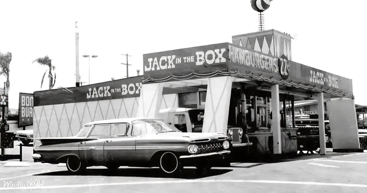 A vintage car is parked in front of a classic Jack-in-the-Box fast-food restaurant.