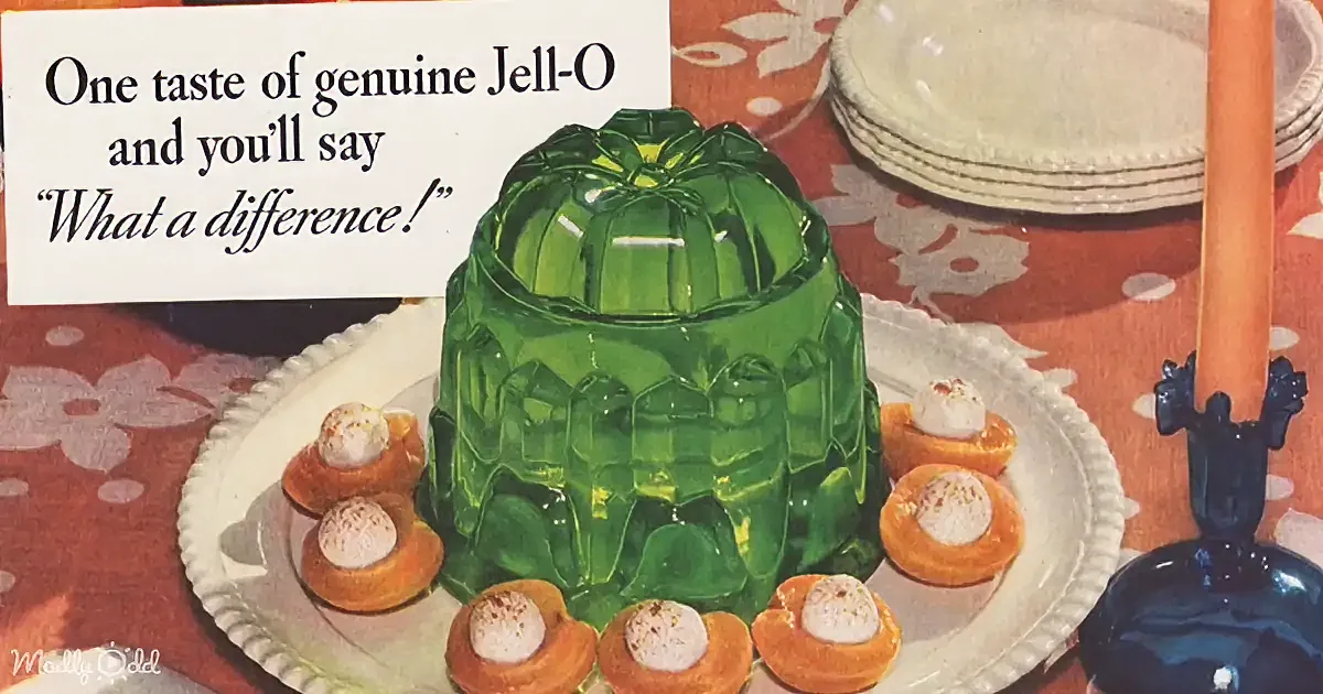 A vibrant green Jell-O mold sits on a plate surrounded by orange dessert cups, with a vintage advertisement in the corner.