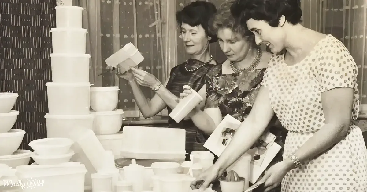 Three women are arranging white plastic containers on a table, with a stack of similar containers in the background.