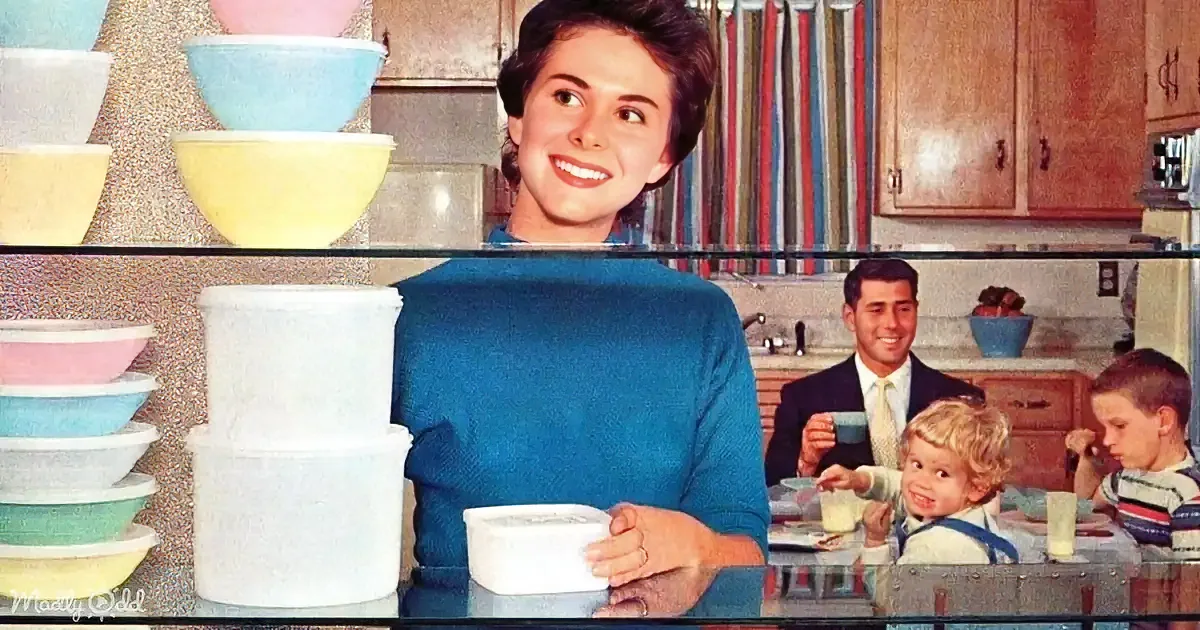 A woman in a blue dress smiles in a kitchen with colorful bowls and a family in the background.