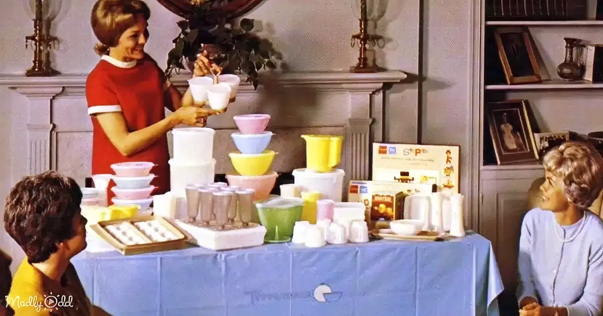 A woman in a red dress stands behind a table displaying colorful plastic bowls and cups, engaging with two children.