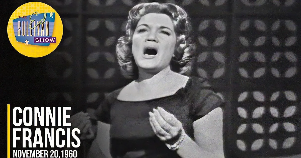 A woman in a black dress with her hands raised, set against a patterned background.