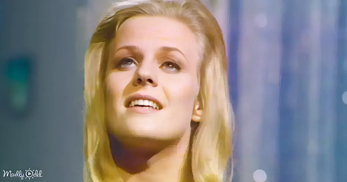 Blonde woman with a warm smile, looking upward, in a softly lit setting.