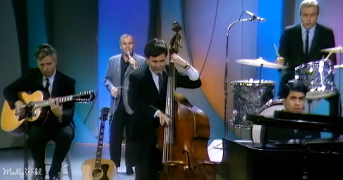 A man in a suit plays a double bass on stage with other musicians.