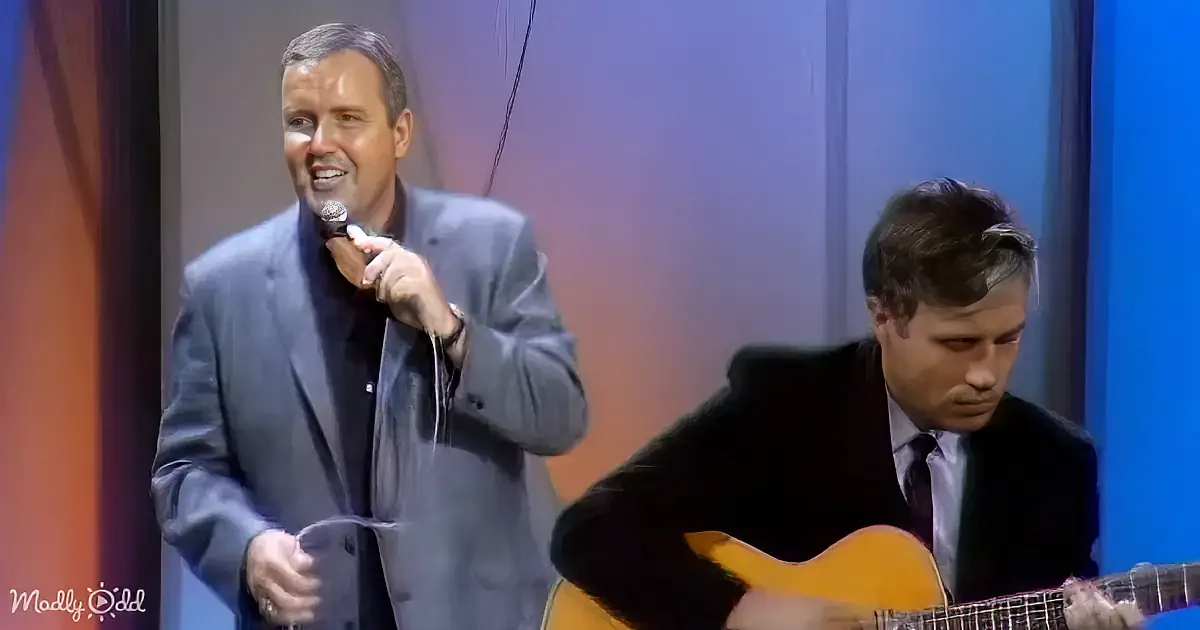 A man in a suit sings into a microphone while another man plays a guitar.
