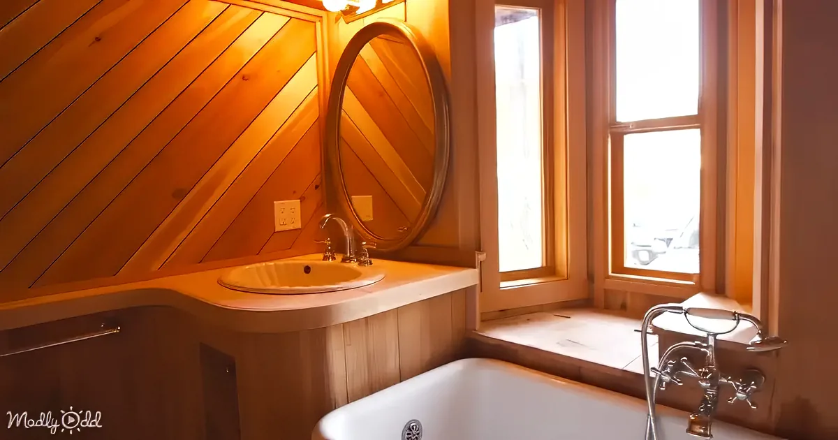 A cozy bathroom with wooden walls, a white sink, a bathtub, and a large window letting in natural light.