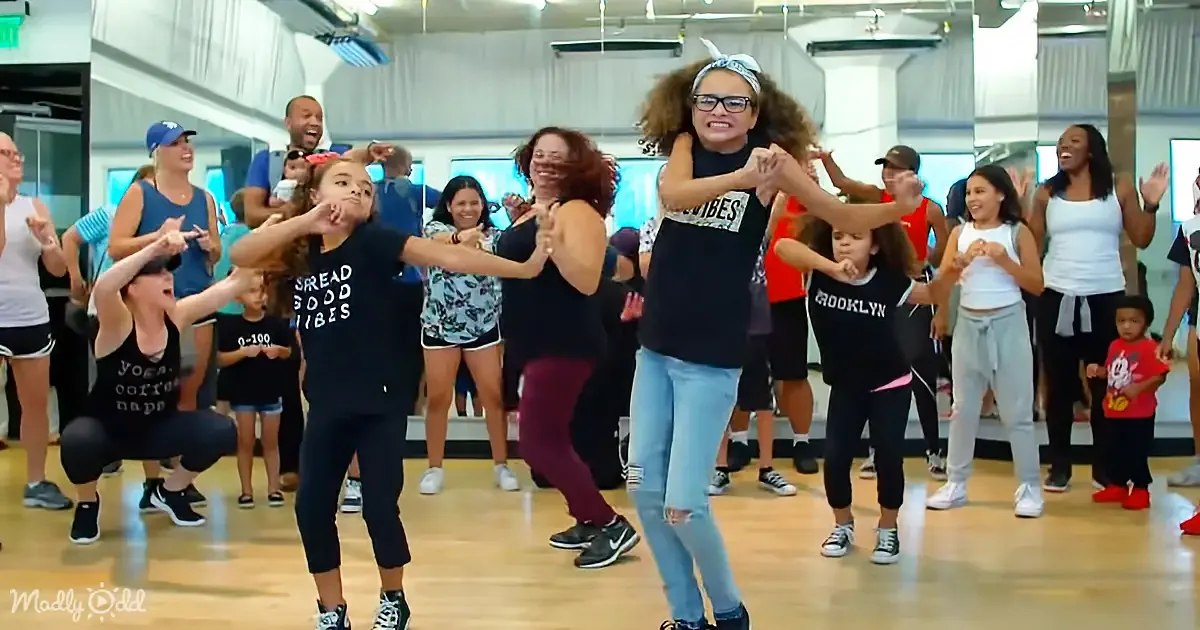 A group of people, including children and adults, are dancing and smiling in a studio.