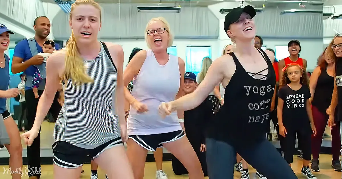 Three women in a dance class, one in a black tank top leading the movement.
