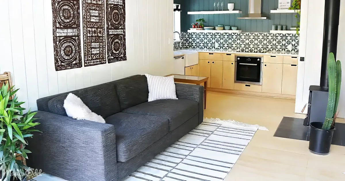 A cozy living room with a dark gray couch, white rug, and a kitchen in the background.