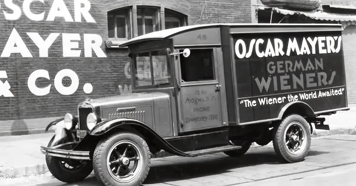 An old Oscar Mayer delivery truck advertises "German Wiener" in front of a brick building.