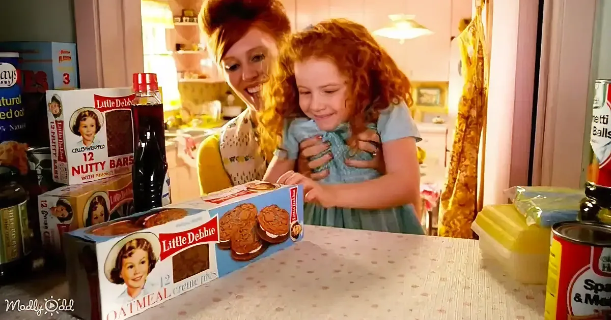 A woman and child smile at Little Debbie oatmeal cream pies on a kitchen counter.