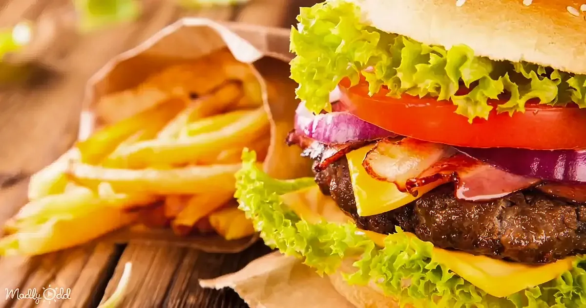 A juicy burger with lettuce, tomato, onion, bacon, and cheese sits next to crispy fries on a wooden table.