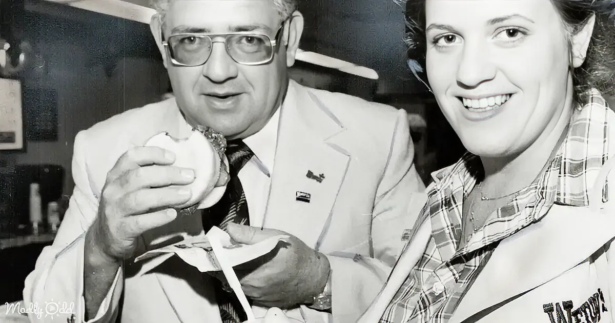 A man in a suit holds a small object, smiling, with a woman beside him.