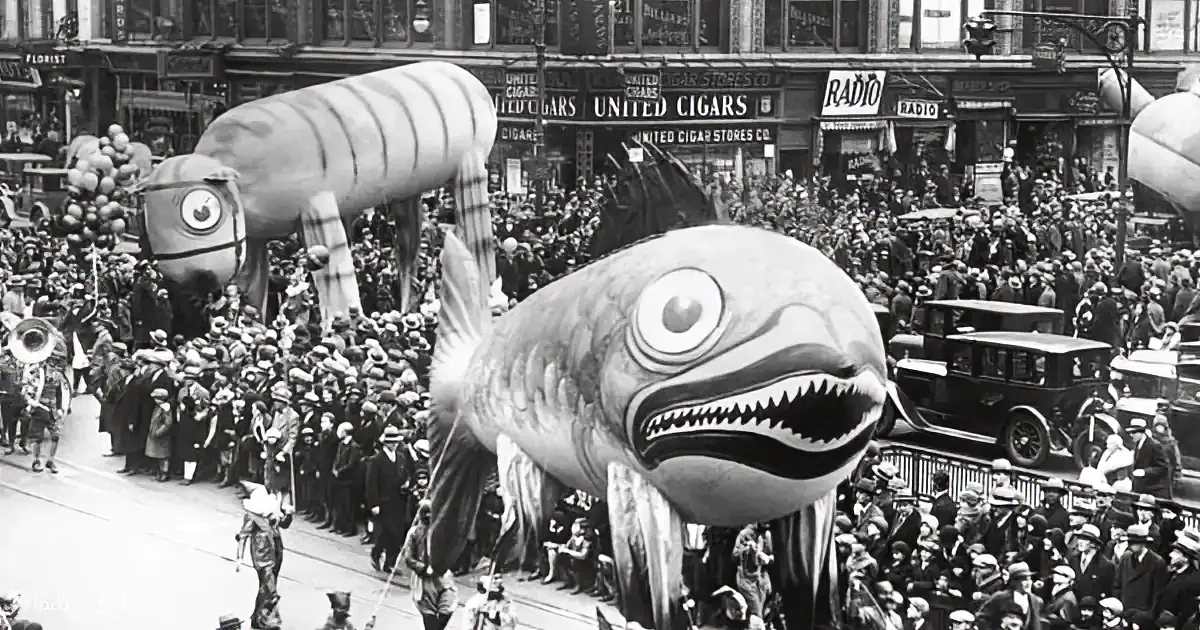 A large, inflatable whale float dominates a bustling parade, drawing a crowd of spectators.