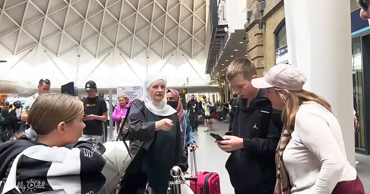 A nun in a black habit and white veil is interacting with a group of people in a busy indoor setting.