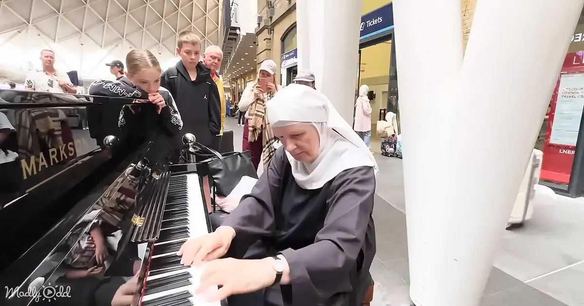 A nun plays a piano in a busy public space, surrounded by onlookers.