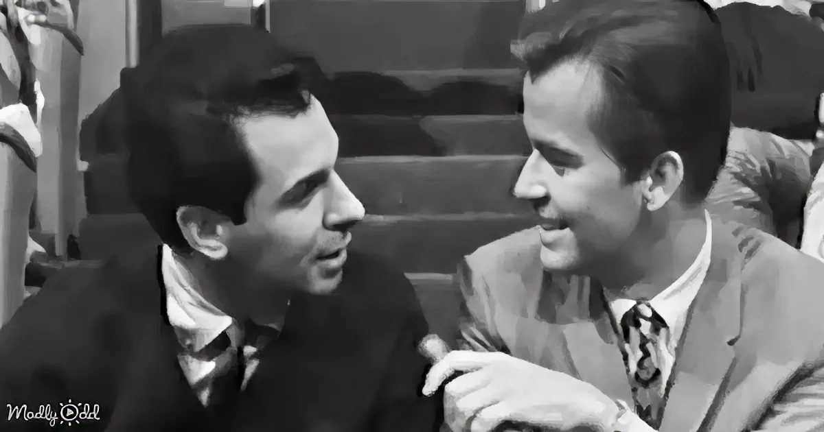 Two men in suits are seated, one leaning forward, both engaged in conversation.