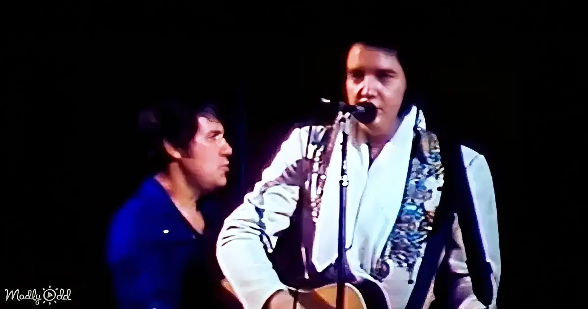 A man in a white sequined jacket sings into a microphone, accompanied by another man in a blue jacket.