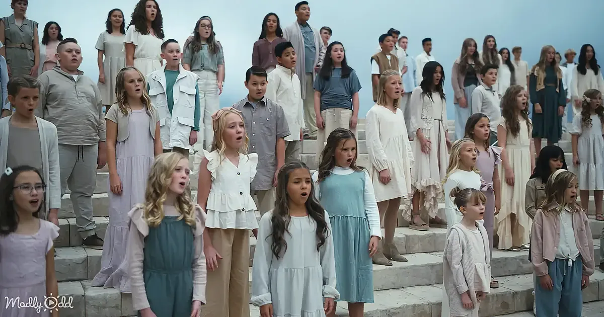 A group of children and adults in a choir setting, singing on stone steps.