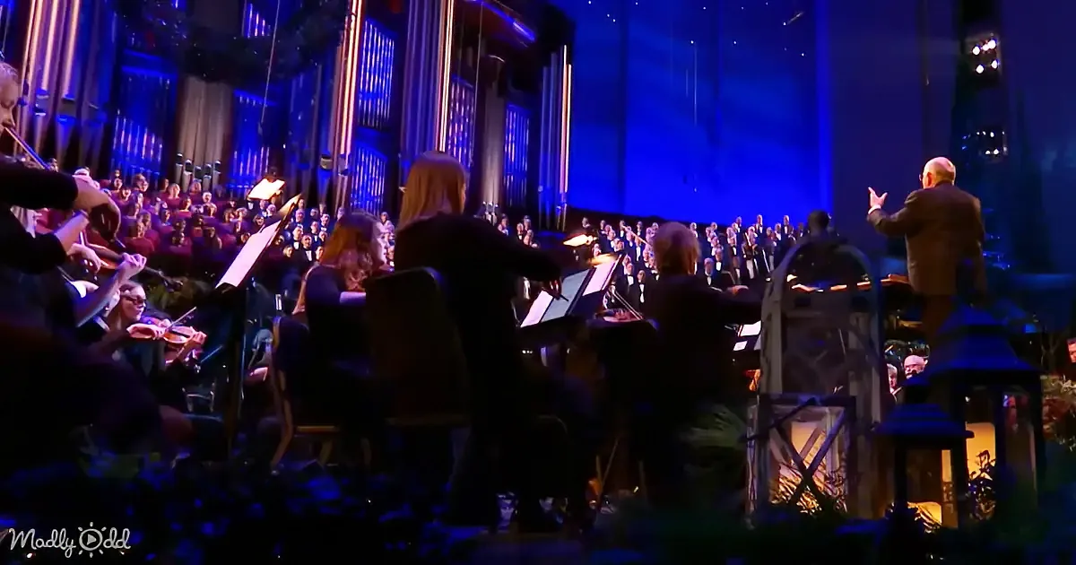 Conductor leads orchestra and choir in a grand performance with blue stage lighting.
