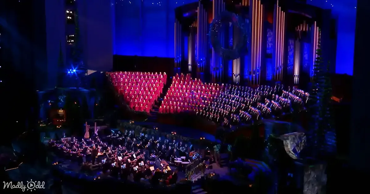 A grand choir and orchestra perform on a stage adorned with Christmas decorations.