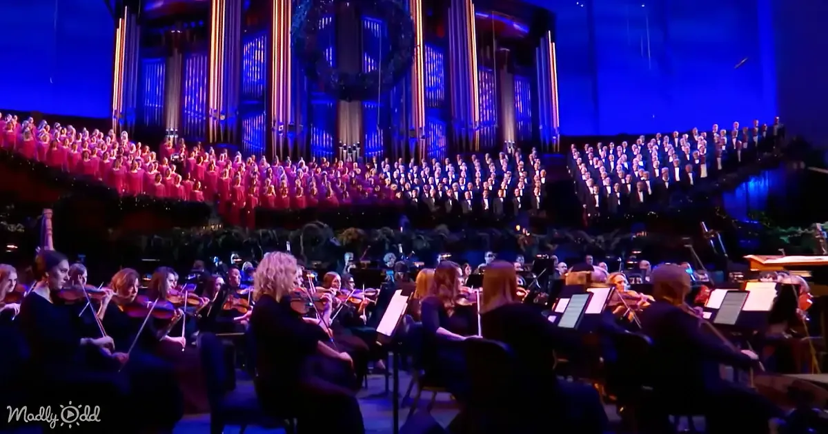 An orchestra and choir perform in a grand hall with blue lighting.