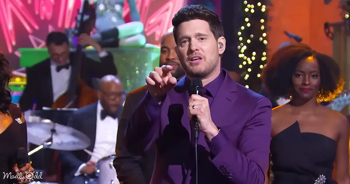 A man in a purple suit sings into a microphone, gesturing with his right hand.
