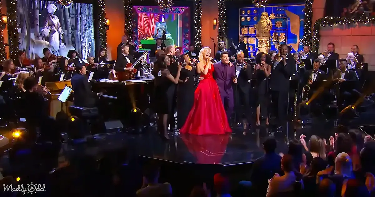 A woman in a red dress sings on stage with a band and choir, surrounded by festive decorations.
