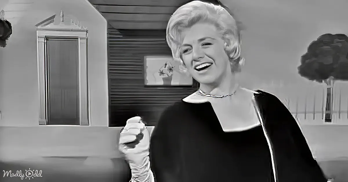 A smiling woman in a black dress and white gloves holds a pastry, set against a black-and-white background with a house...