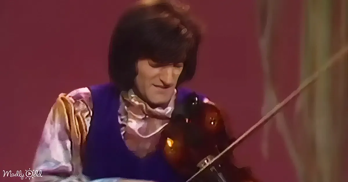 A person in a colorful outfit plays a violin against a red background.