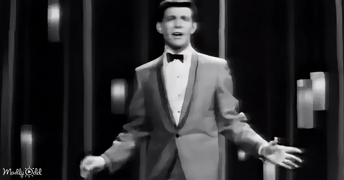 A man in a tuxedo with a bow tie and hat is singing with his arms outstretched.