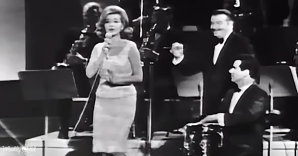 A woman in a dress sings into a microphone on stage with a band.