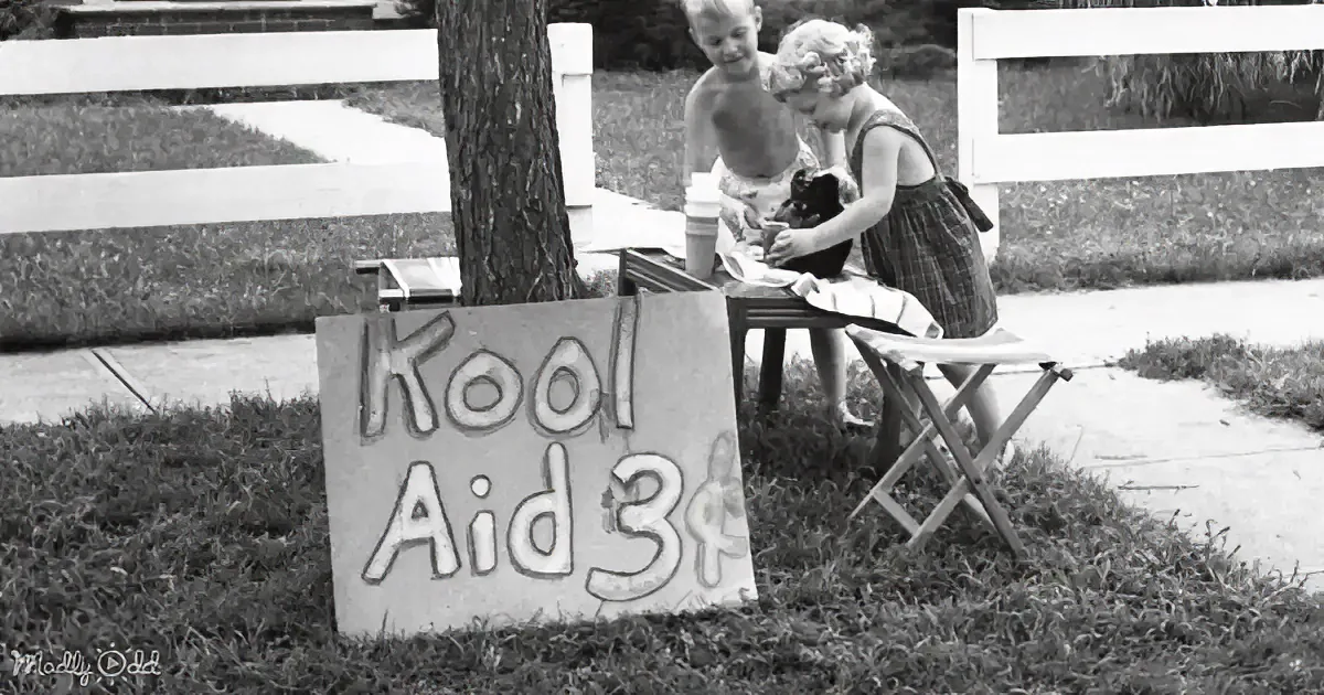 Children selling Kool Aid at a roadside stand with a sign indicating the price.