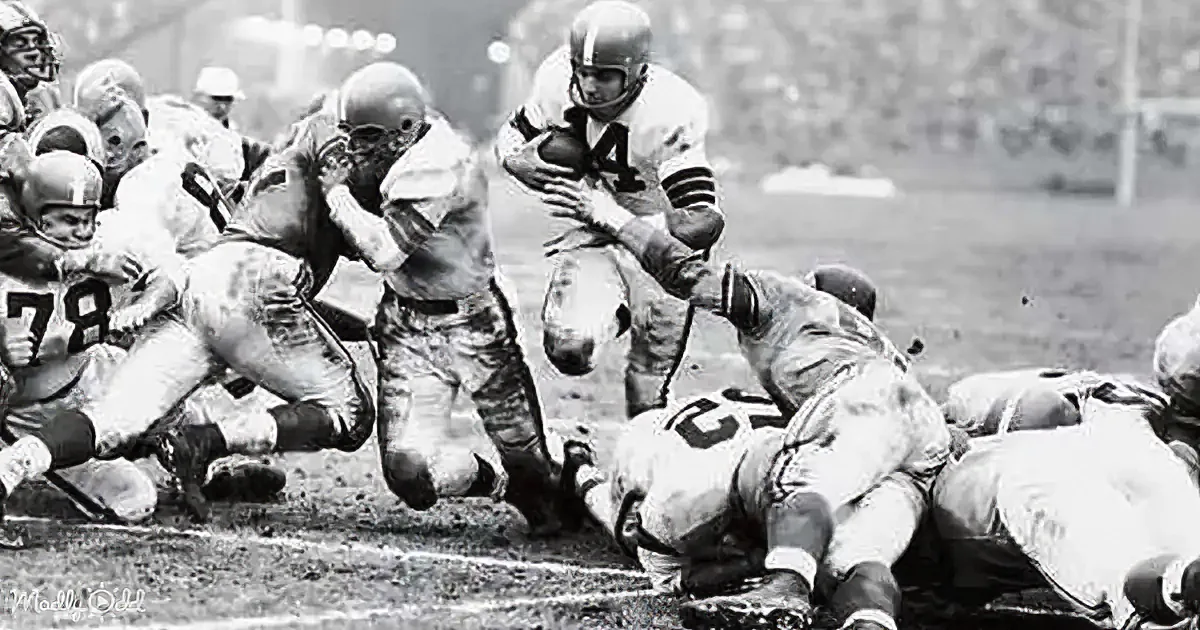 Quarterback in white jersey runs with football, surrounded by opposing players in a muddy field.