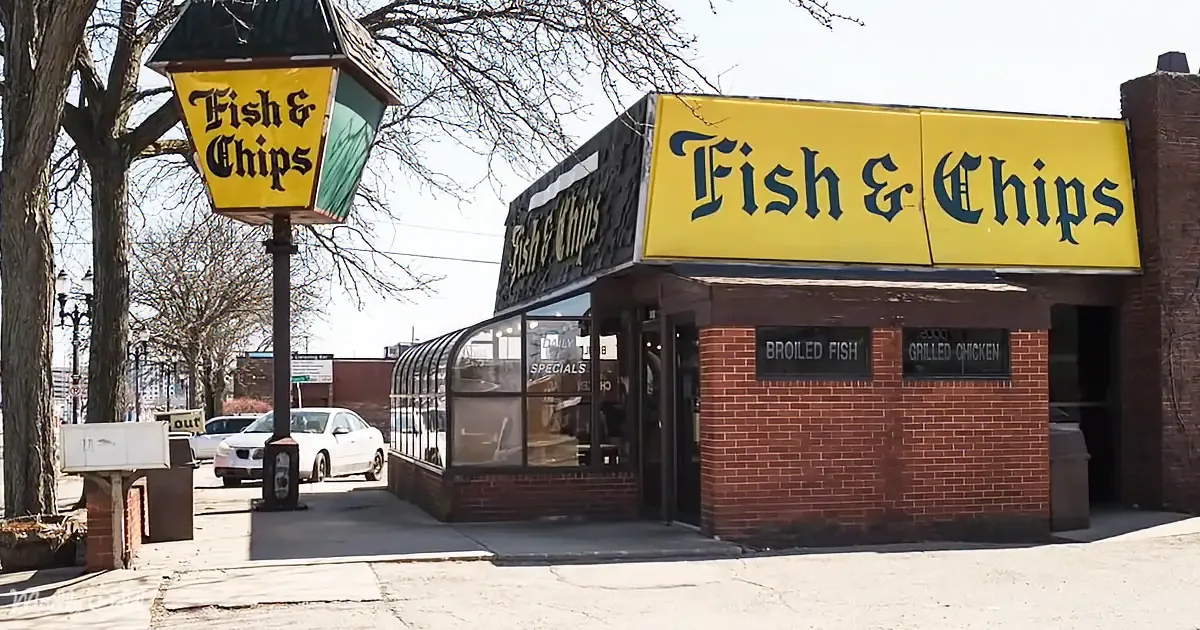 A fish and chips restaurant with a yellow sign and brick facade, located on a sunny day.