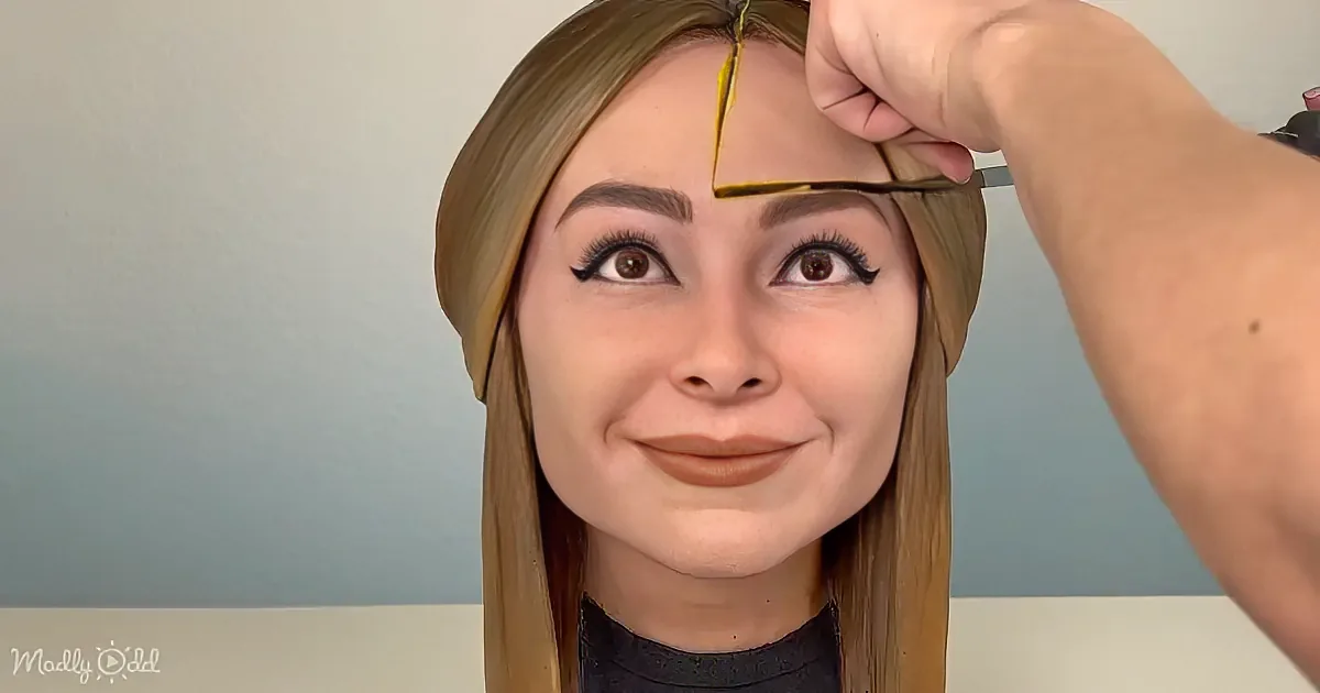 A person with long blonde hair is having yellow paint applied to their forehead by another person.