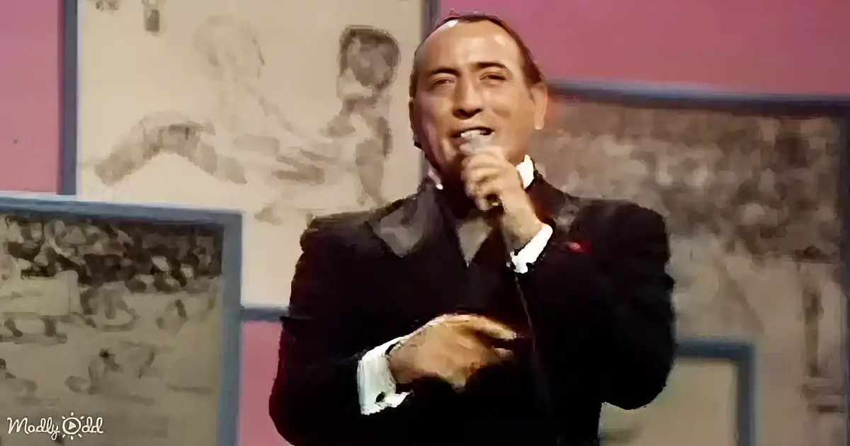 A man in a suit holds a microphone, singing on stage with a backdrop of sketches.