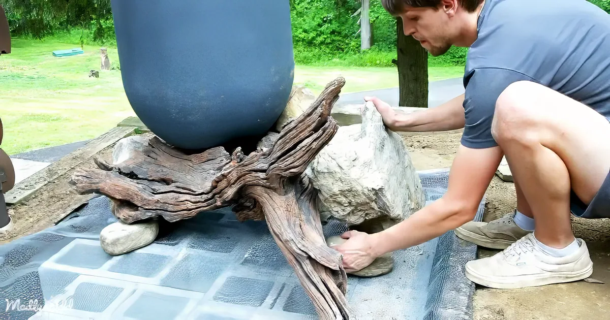 A man is carefully arranging rocks and driftwood on a mat, preparing a garden feature.