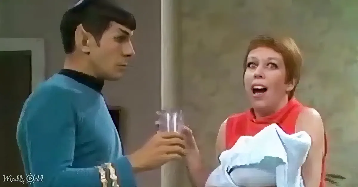 Spock in blue uniform holds a glass, while a woman in red dress looks surprised, holding a white cloth.