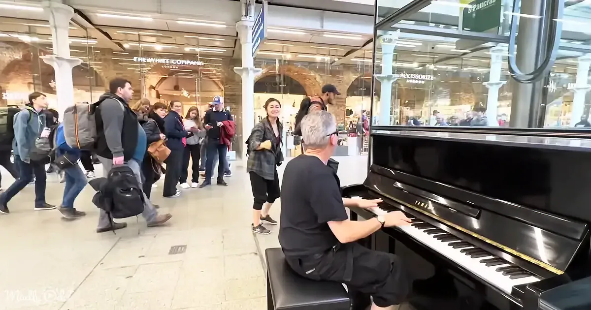 A man plays a piano in a busy train station, surrounded by people walking by.